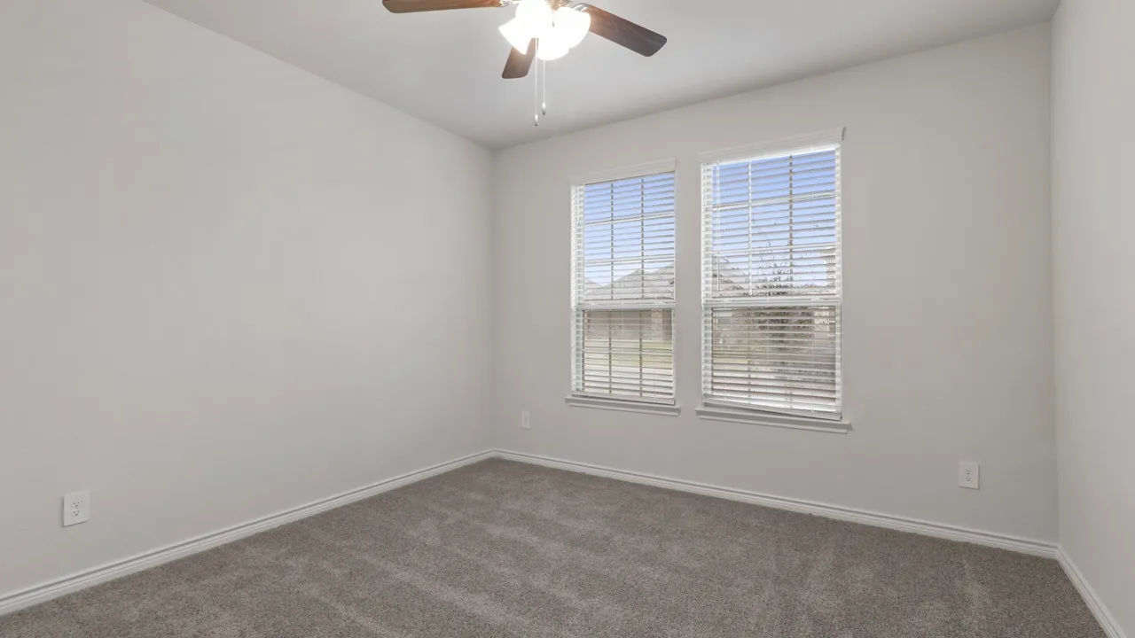 Bright secondary bedroom with double-hung windows featuring plantation shutters, neutral wall finishes, and plush carpet flooring