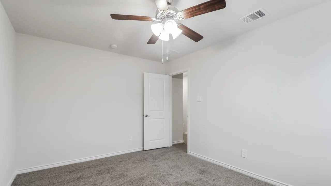 Spacious bedroom featuring neutral wall finishes, carpeted flooring, a ceiling fan with integrated lighting, and a white six-panel closet door providing ample storage