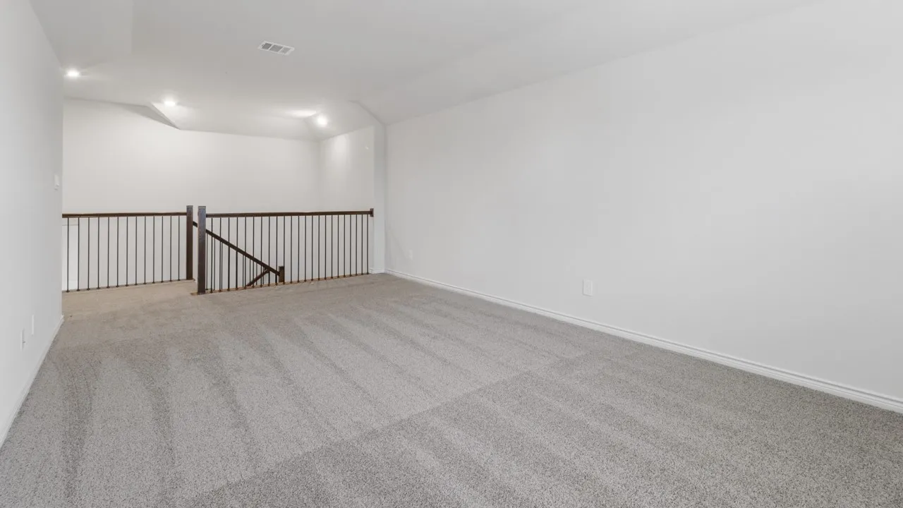 Spacious carpeted bonus room featuring a dark wood newel post and railings with black metal spindles, recessed lighting, and white baseboards
