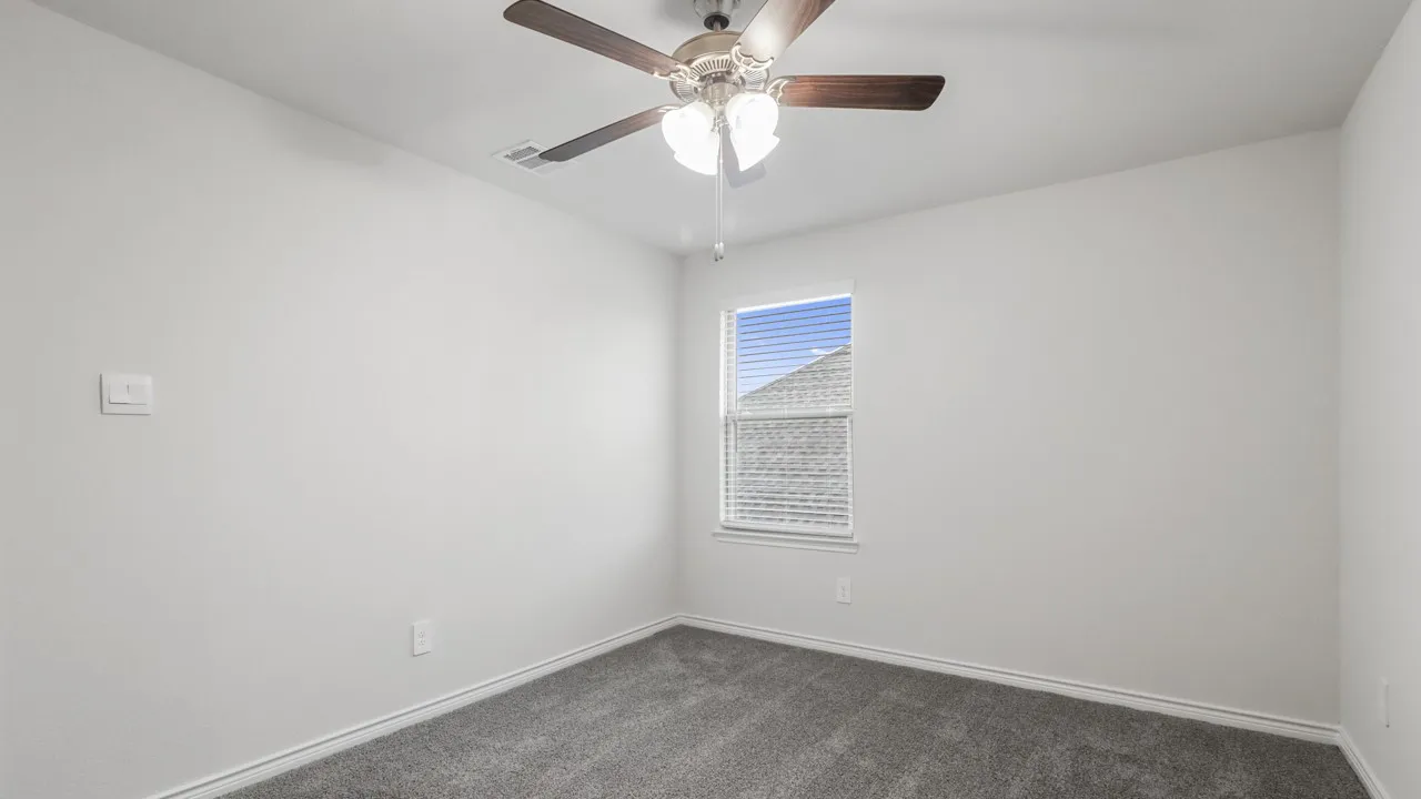 Neutral wall finishes with a single window featuring blinds, dark gray carpet, a ceiling fan with light fixture, and white baseboards