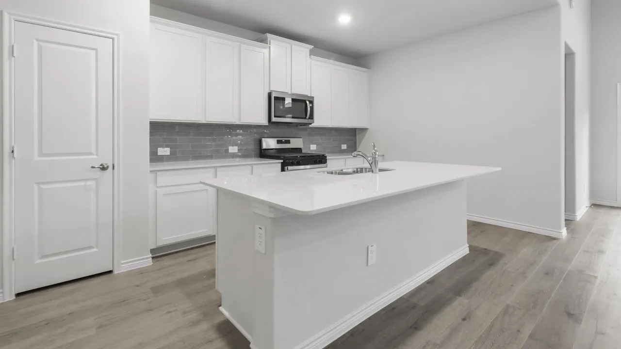 Modern kitchen featuring white cabinetry, a large waterfall-edge island with white quartz countertop, stainless steel appliances including a built-in microwave, gray subway tile backsplash, and wood-finish flooring throughout
