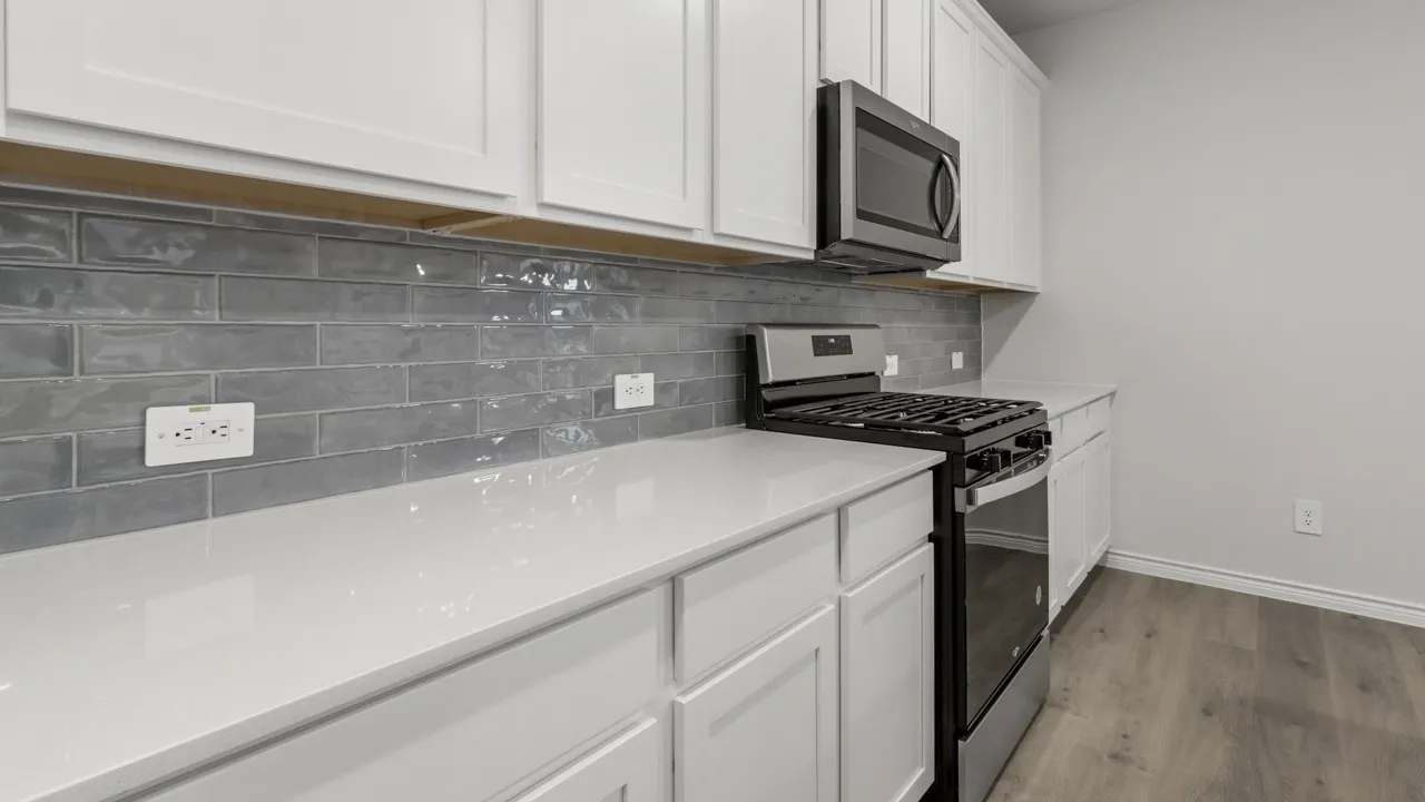 Modern kitchen featuring white shaker-style cabinetry, white quartz countertops with undermount sink, stainless steel gas range with black finish, integrated microwave, gray subway tile backsplash, and wood-finish flooring throughout