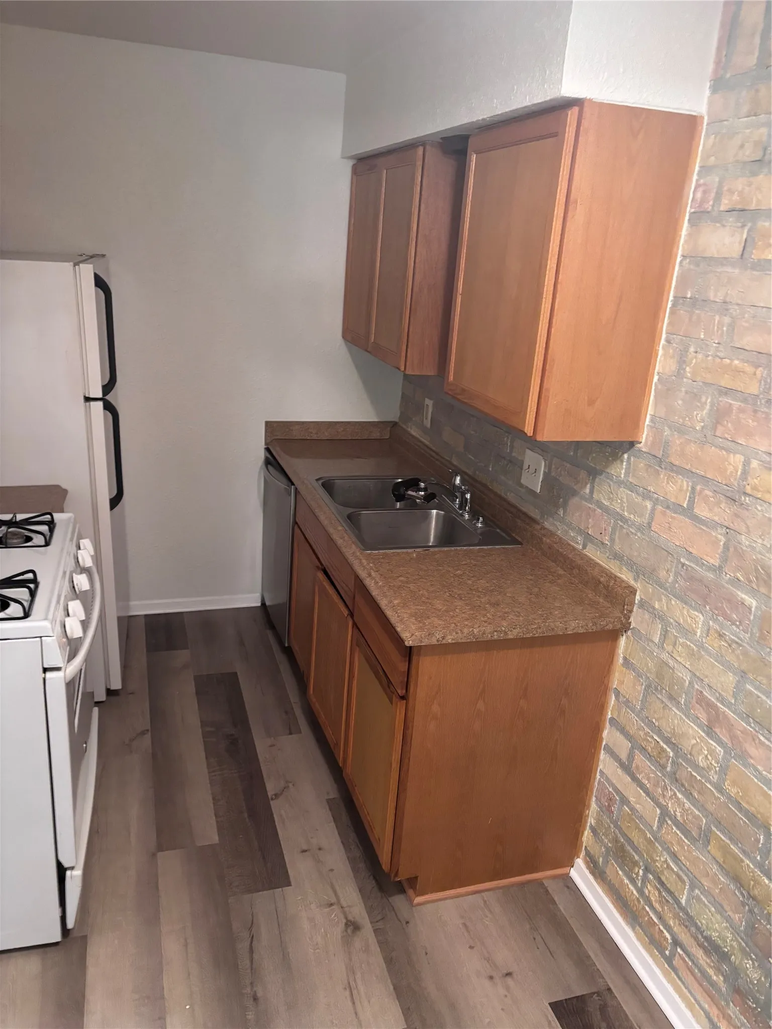 Galley kitchen featuring warm wood-finish cabinetry, granite countertops, stainless steel sink with faucet, and wood-finish flooring