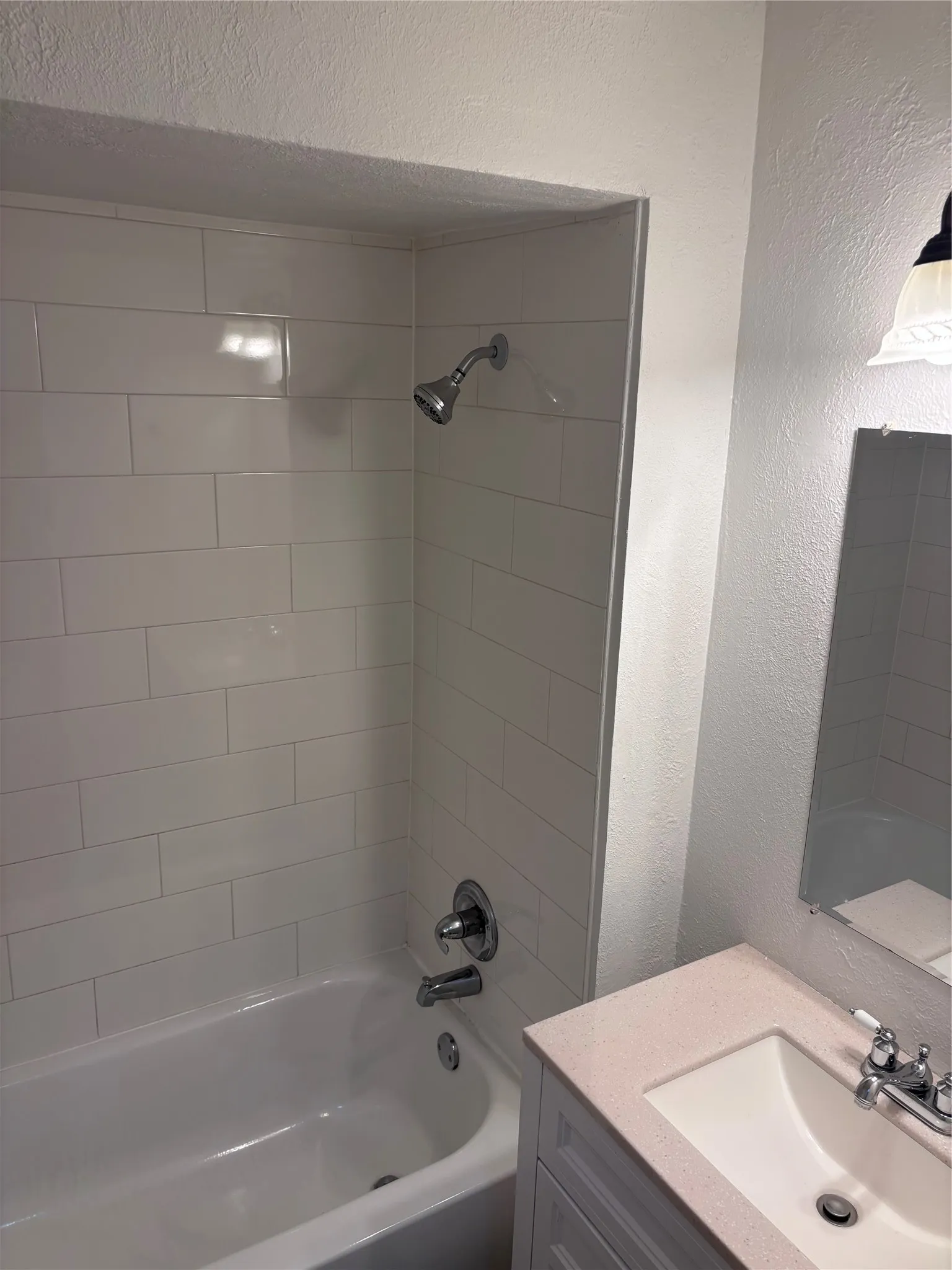 Bathroom featuring a white subway tile shower surround with chrome fixtures, a classic white bathtub, a single vanity with a light-colored countertop, and a mirrored wall