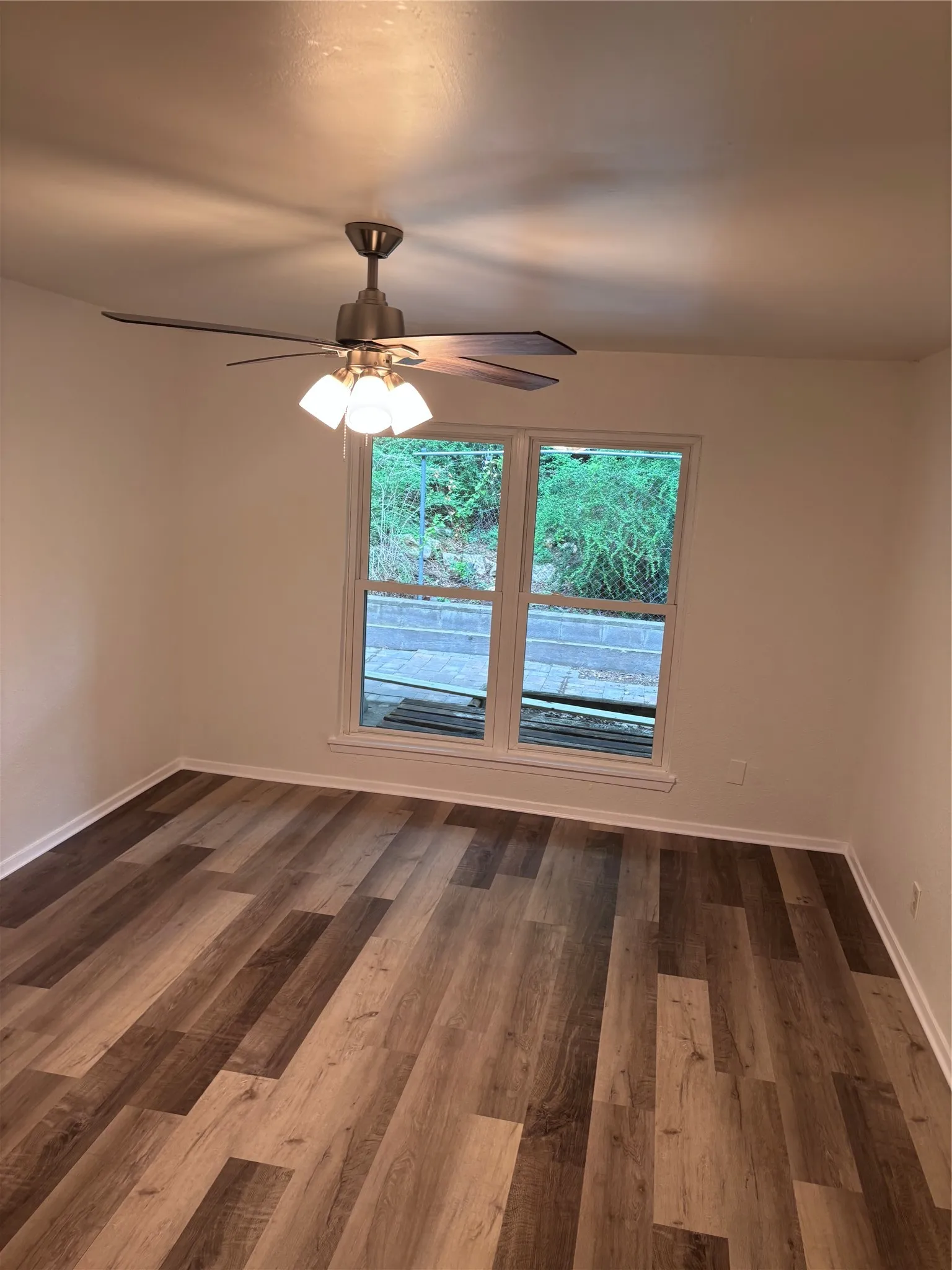Room with wood-finish flooring, white baseboards, and a single window with white trim
