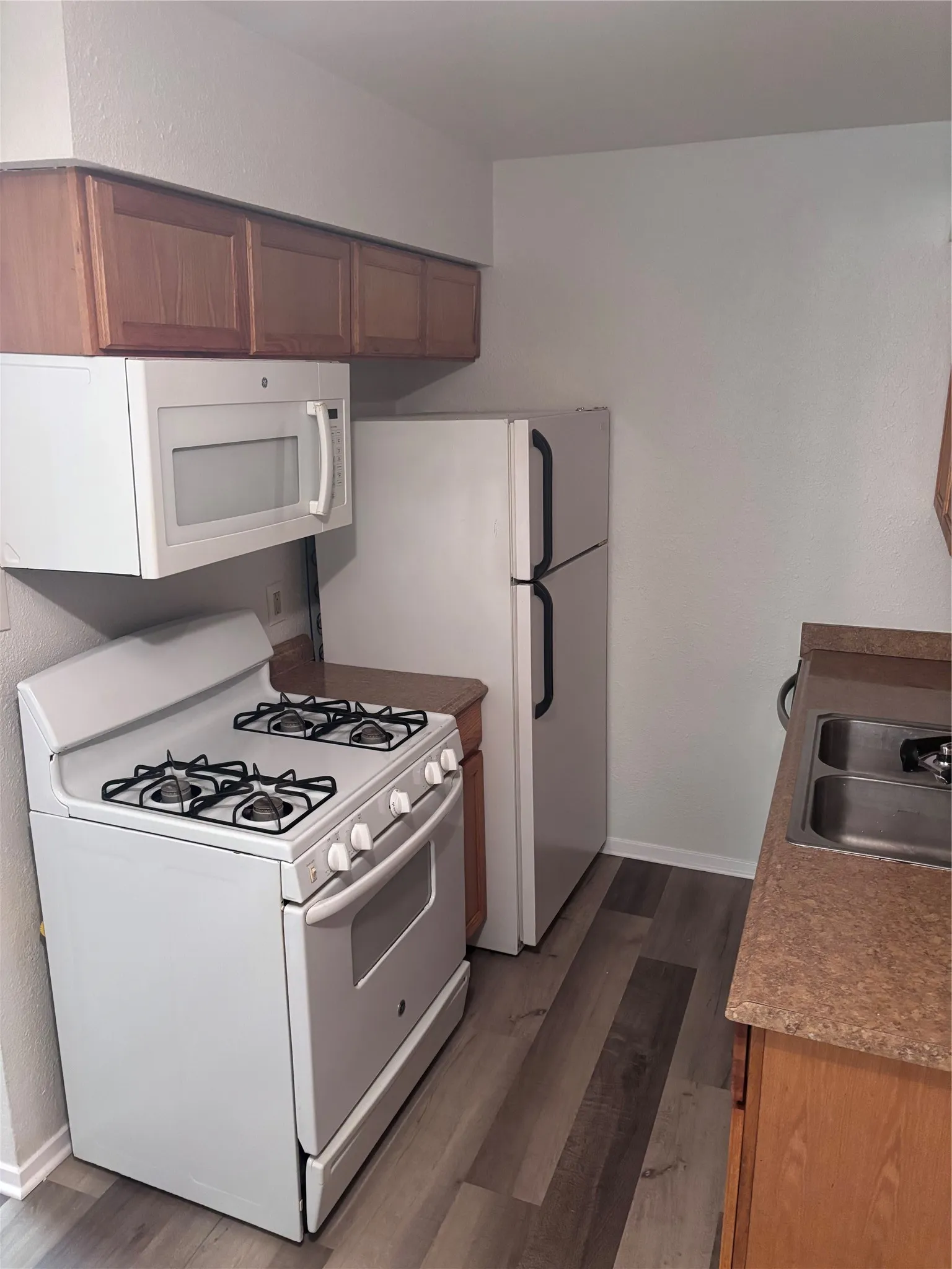 Galley kitchen featuring white appliances including a gas range with four burners, built-in microwave, and refrigerator