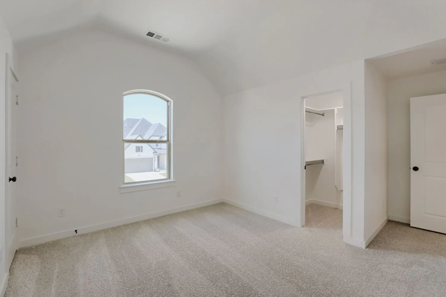 Bright corner bedroom with arched window, neutral carpet flooring, and dual closet access