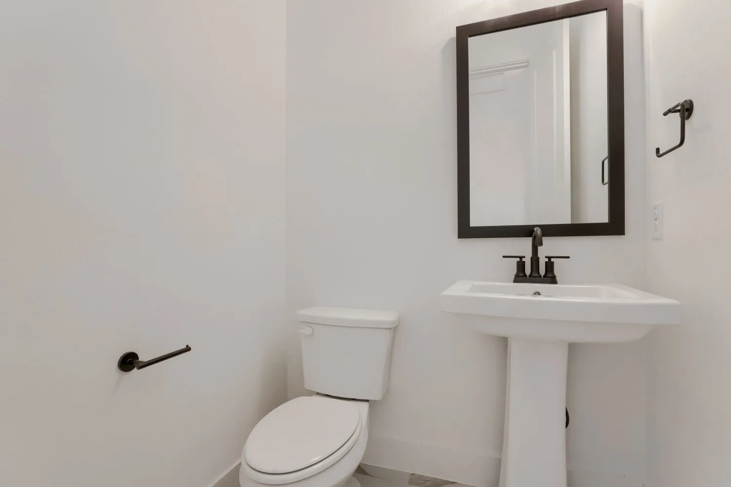Pedestal sink with dark bronze faucet, framed mirror, and coordinating hardware