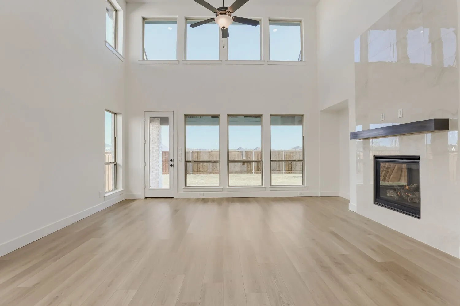 Vaulted ceiling with a ceiling fan, light wood-finish flooring, and multiple windows