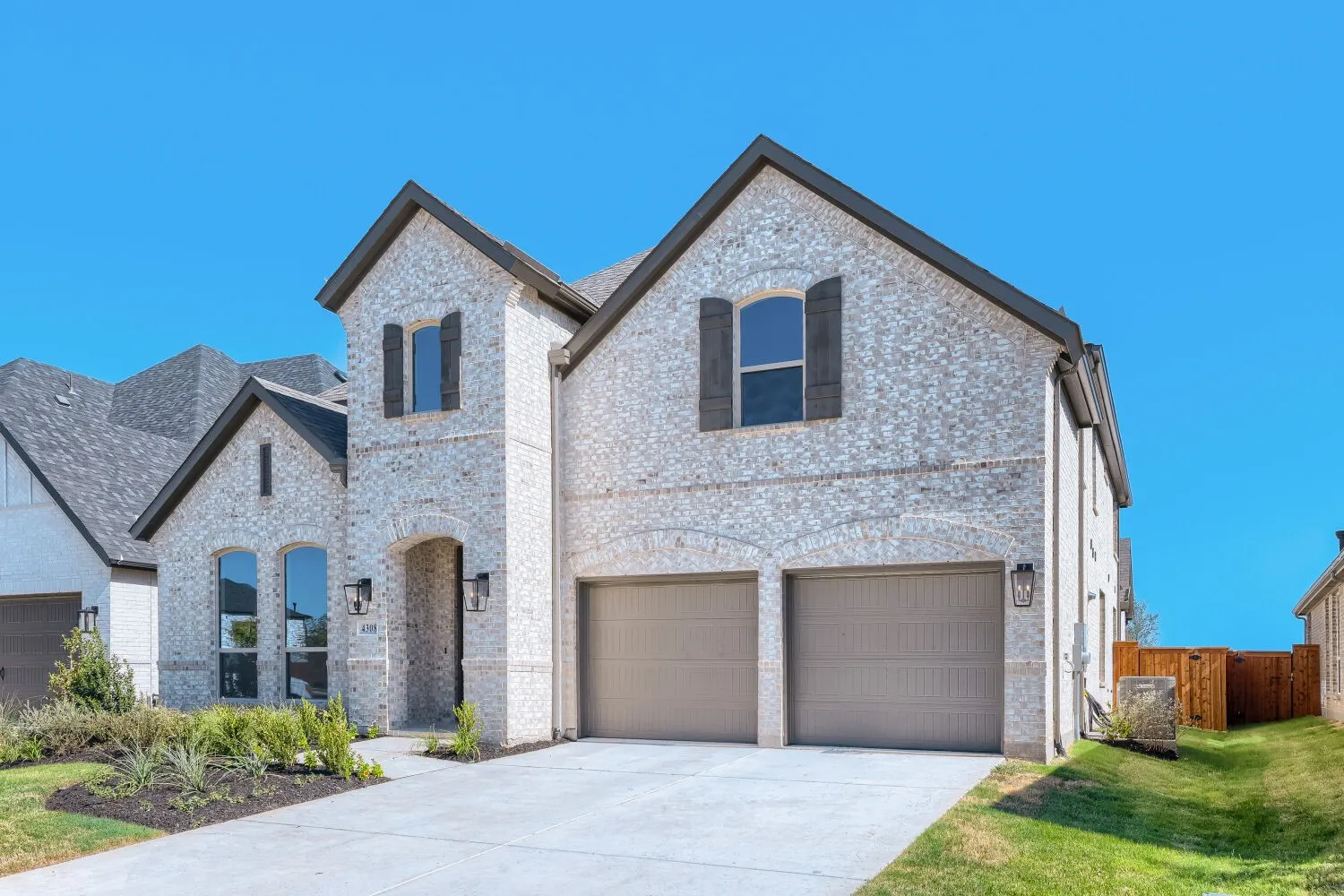 Modern brick and stone two-story residence featuring a prominent front-facing two-car garage with paneled doors, multiple gabled rooflines with architectural depth, and large multi-pane windows throughout the primary and upper facades