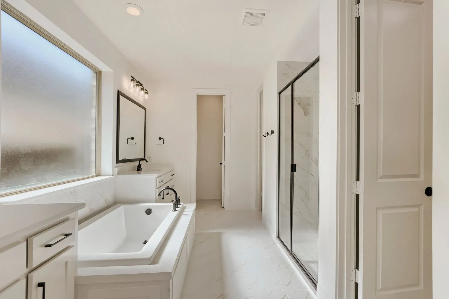 Soaking tub with surrounding white cabinetry and a large frosted window