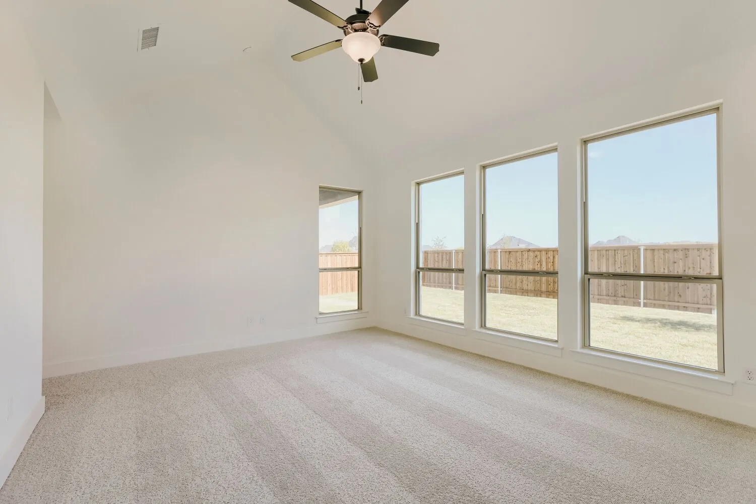 Vaulted ceiling with an attached ceiling fan, large windows, and neutral carpeting