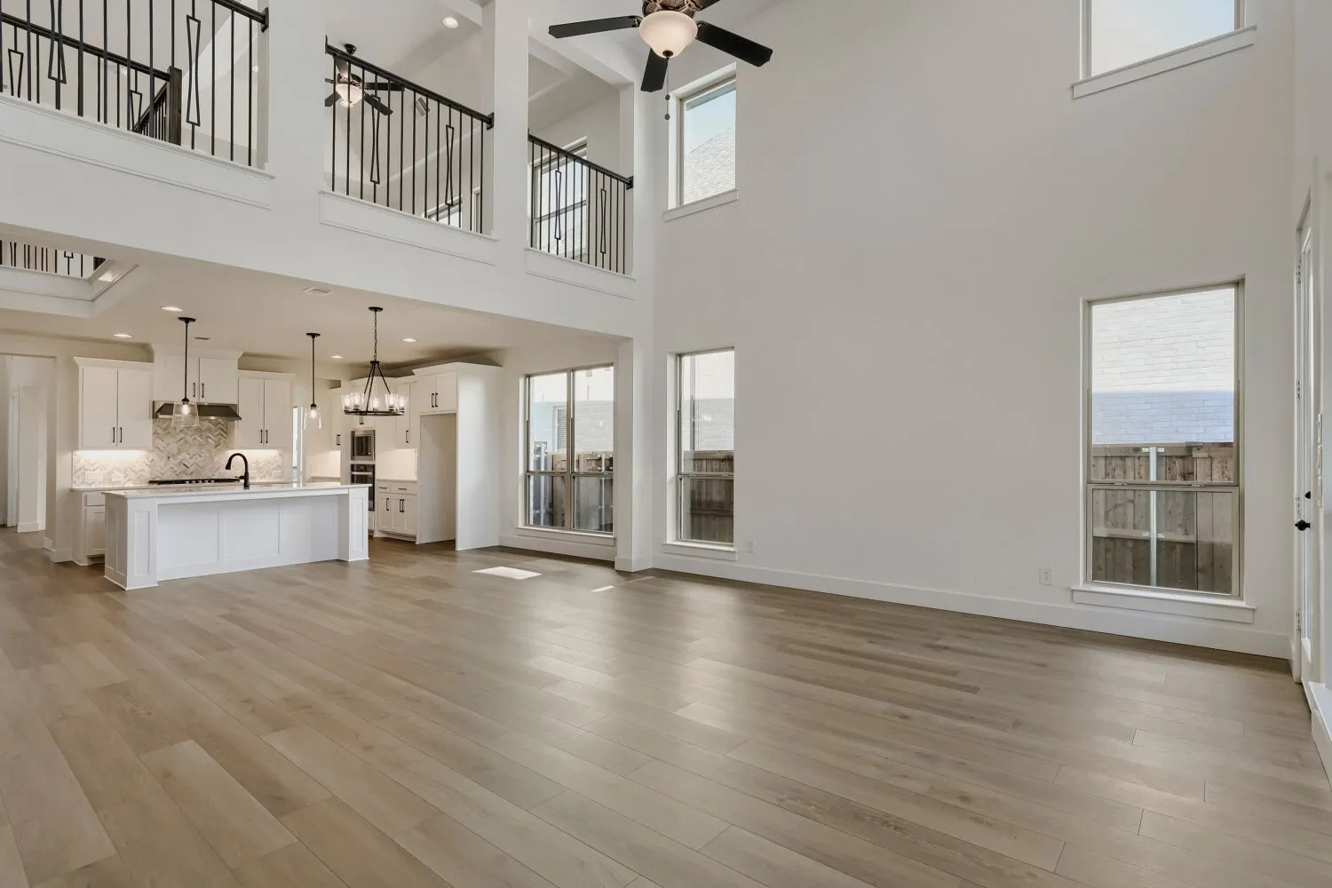 Soaring ceilings, wood-finish flooring, white kitchen cabinetry with a central island, and modern pendant lighting