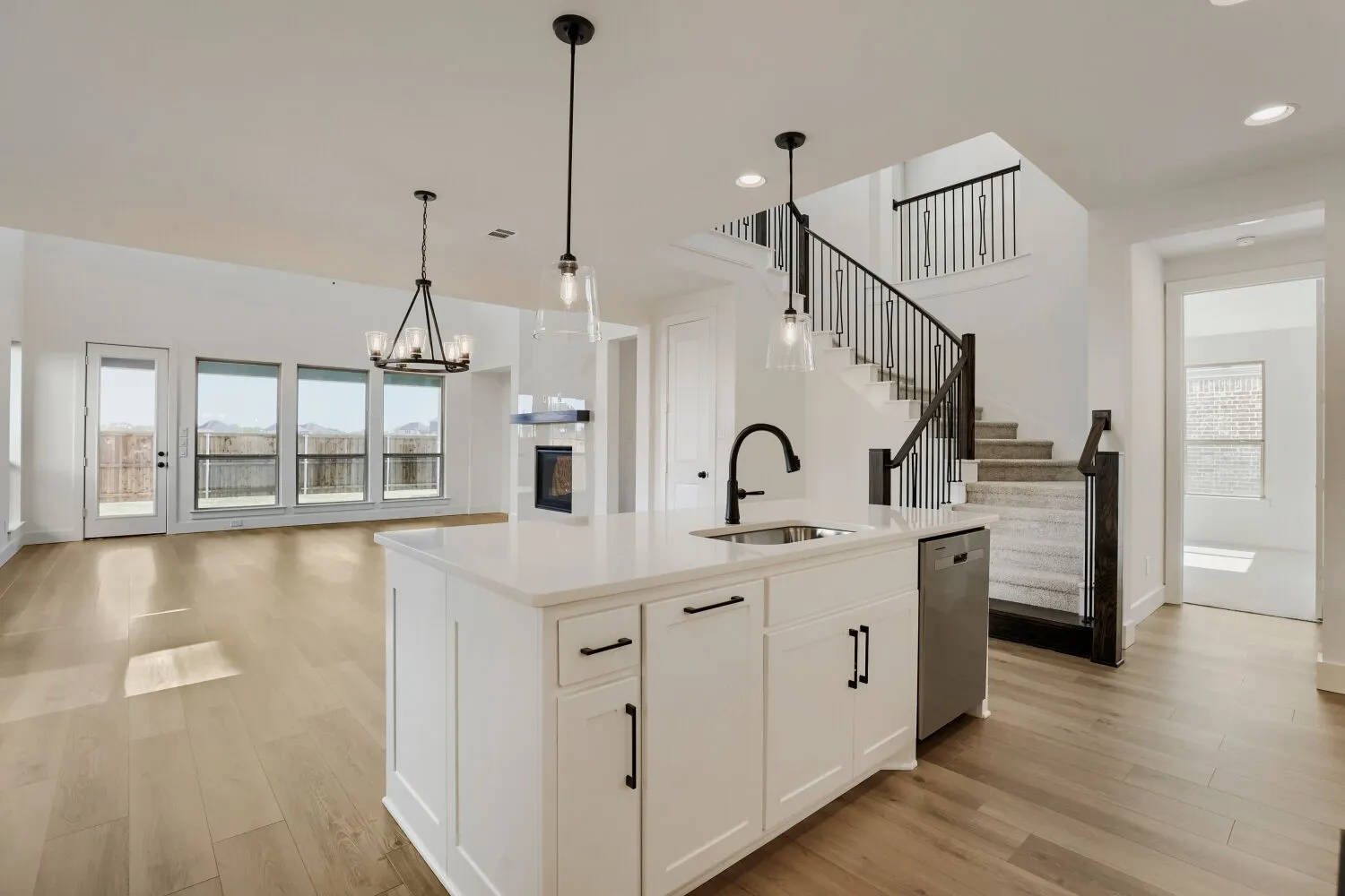 Open-concept living area featuring wood-finish flooring, a kitchen island with stone countertop, a built-in fireplace, and a curved staircase with wrought iron balusters