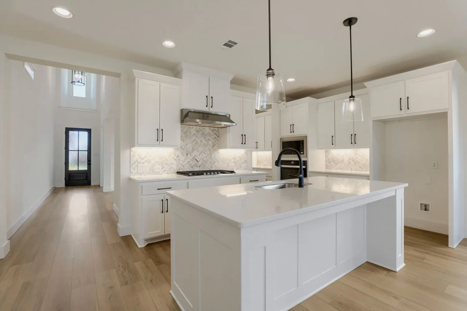 White shaker cabinetry, light wood-finish flooring, recessed lighting, and a kitchen island with pendant lighting