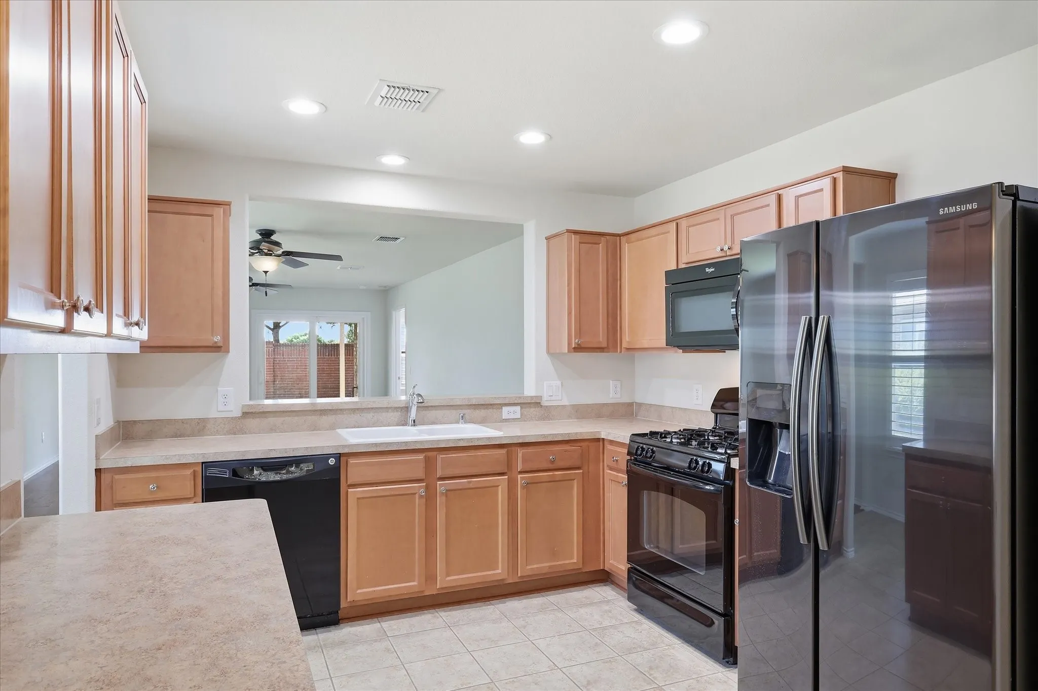 Spacious kitchen featuring warm wood cabinetry, black appliances including a gas range and refrigerator, laminate countertops, recessed lighting, tile flooring