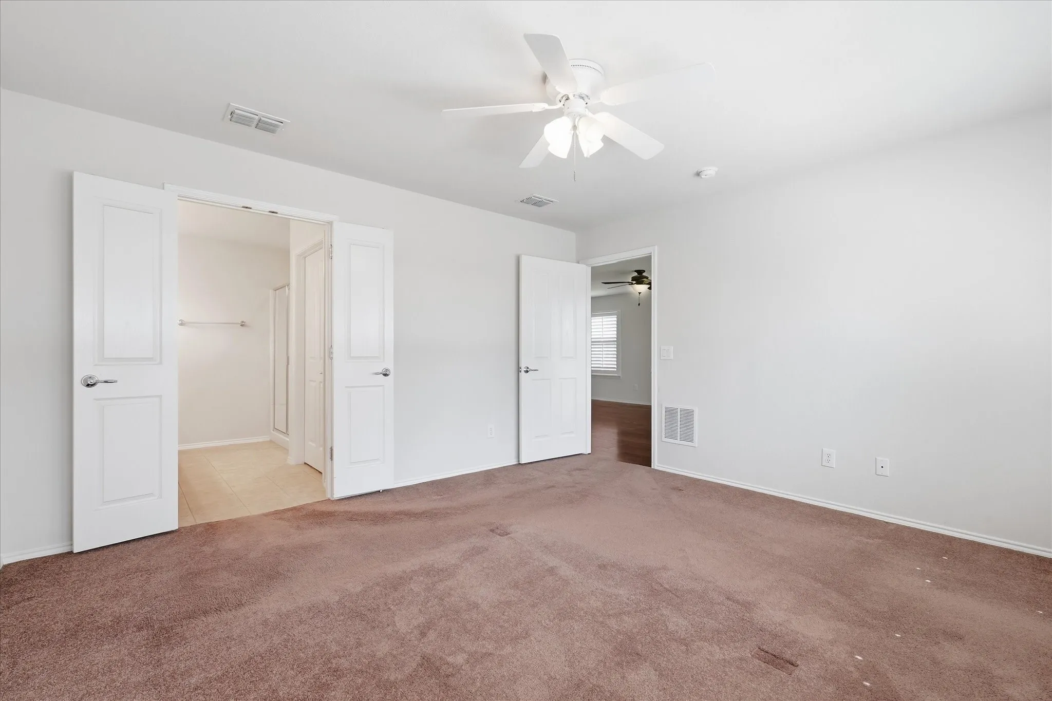 Spacious primary bedroom with carpet flooring, ceiling fan with integrated lighting, and ensuite bathroom including a walk-in closet