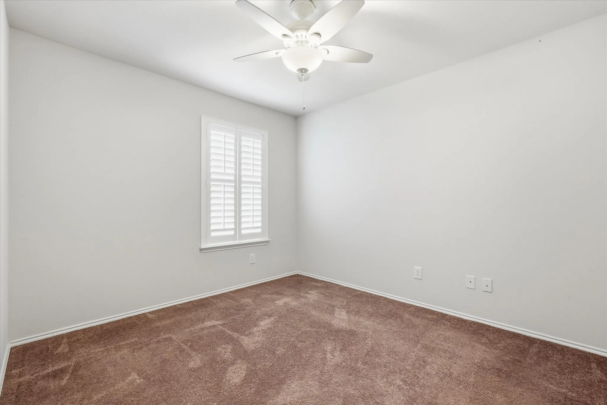 Neutral wall tones with a ceiling fan, window with white plantation shutters, and textured carpet flooring