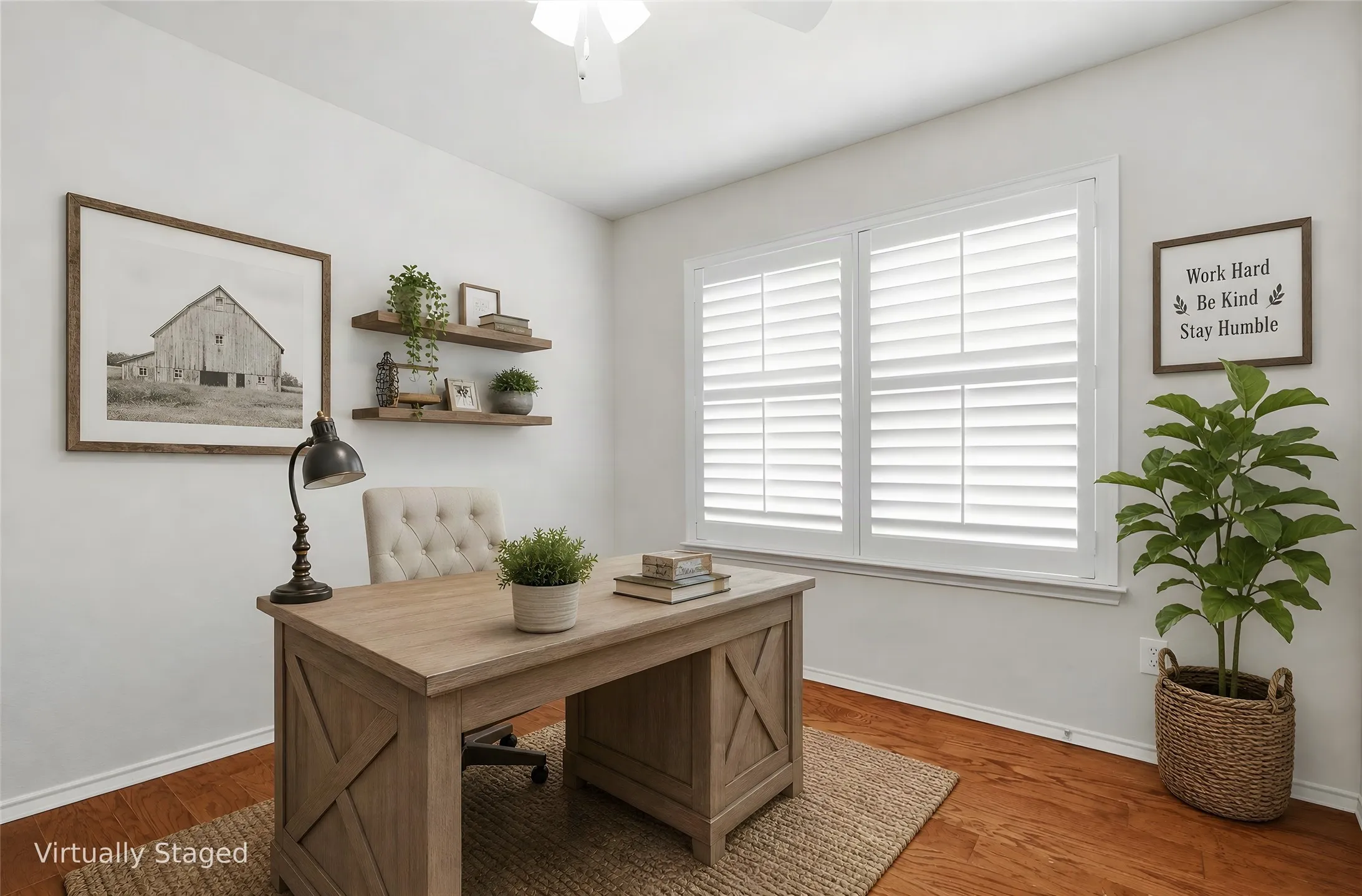 Dedicated home office or bedroom featuring a wood-finish desk with X-panel detailing, hardwood flooring, and large plantation shutter windows allowing natural light