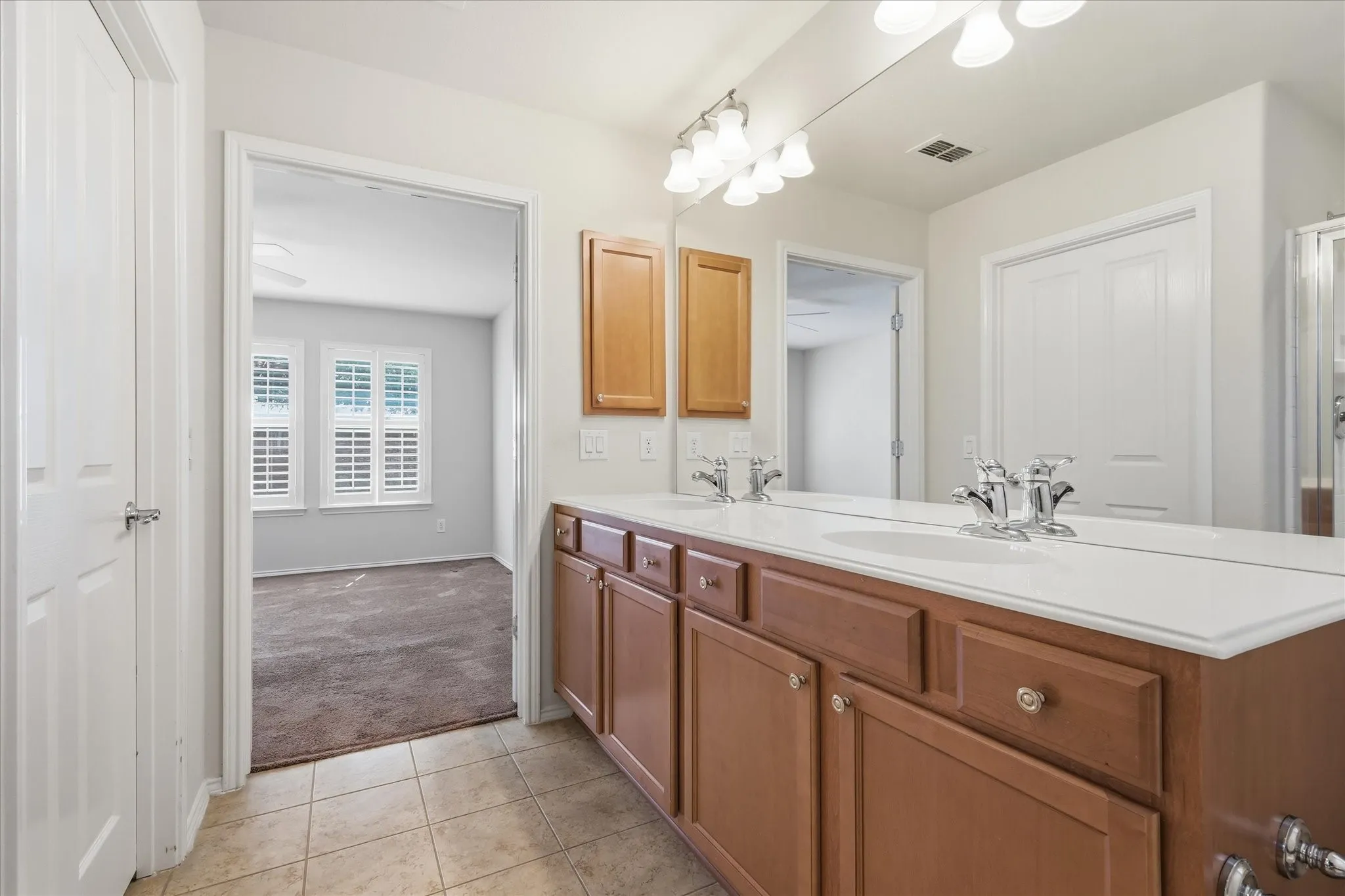 Spacious Primary bathroom featuring a dual vanity with wood-finish cabinetry, white countertop, and chrome fixtures