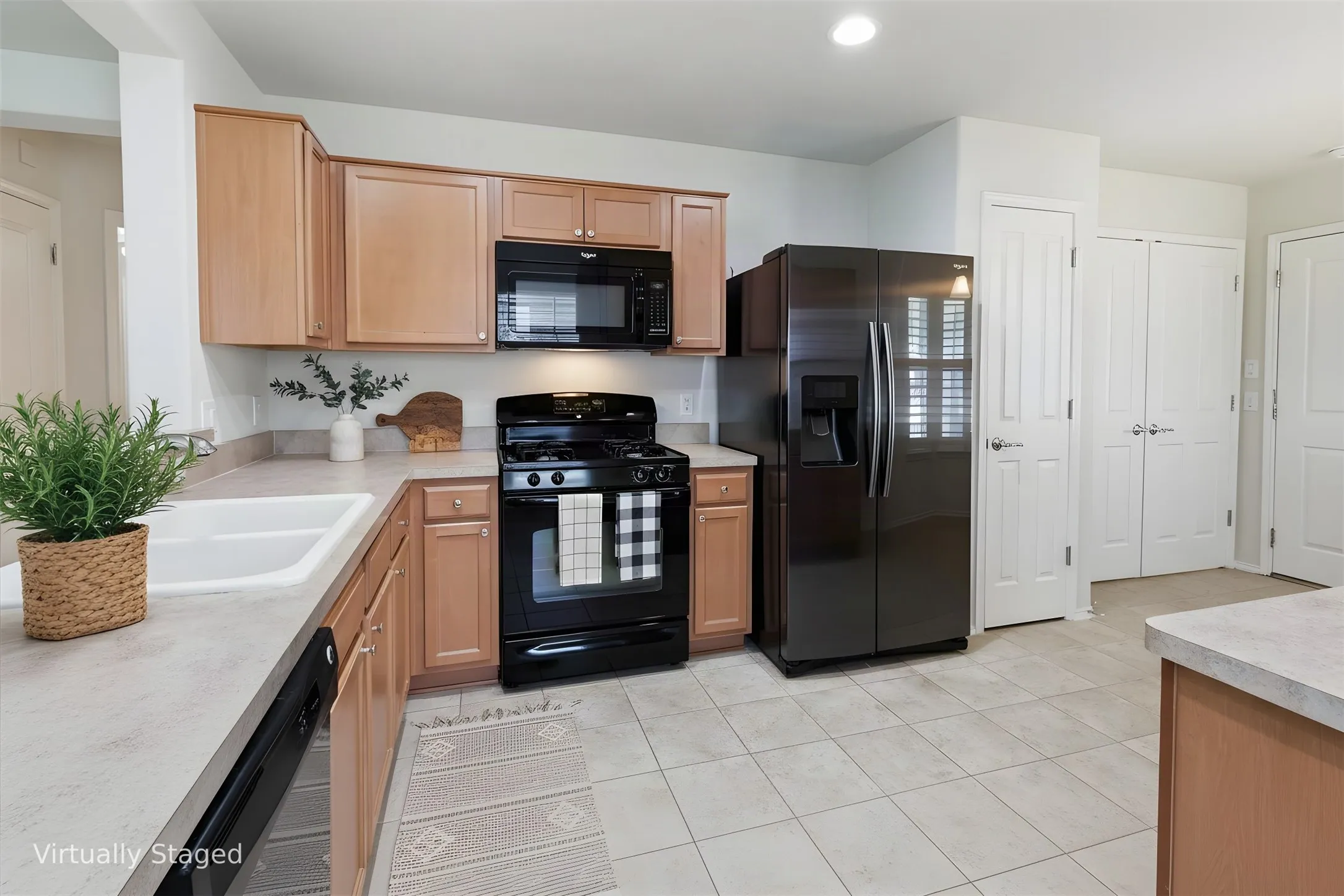 Kitchen featuring light wood cabinetry, light-toned countertops, tile flooring, black appliances, and the Utility Room