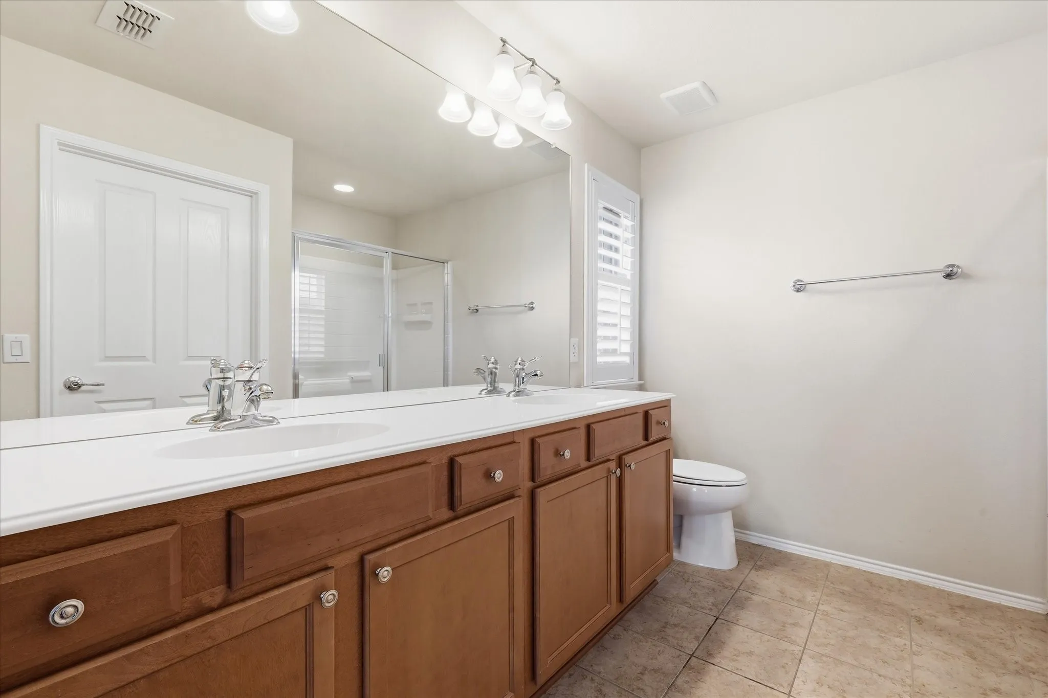 Spacious primary bathroom showcasing a wood-finish vanity with dual sinks, extensive white quartz countertop, and large framed mirror with integrated lighting