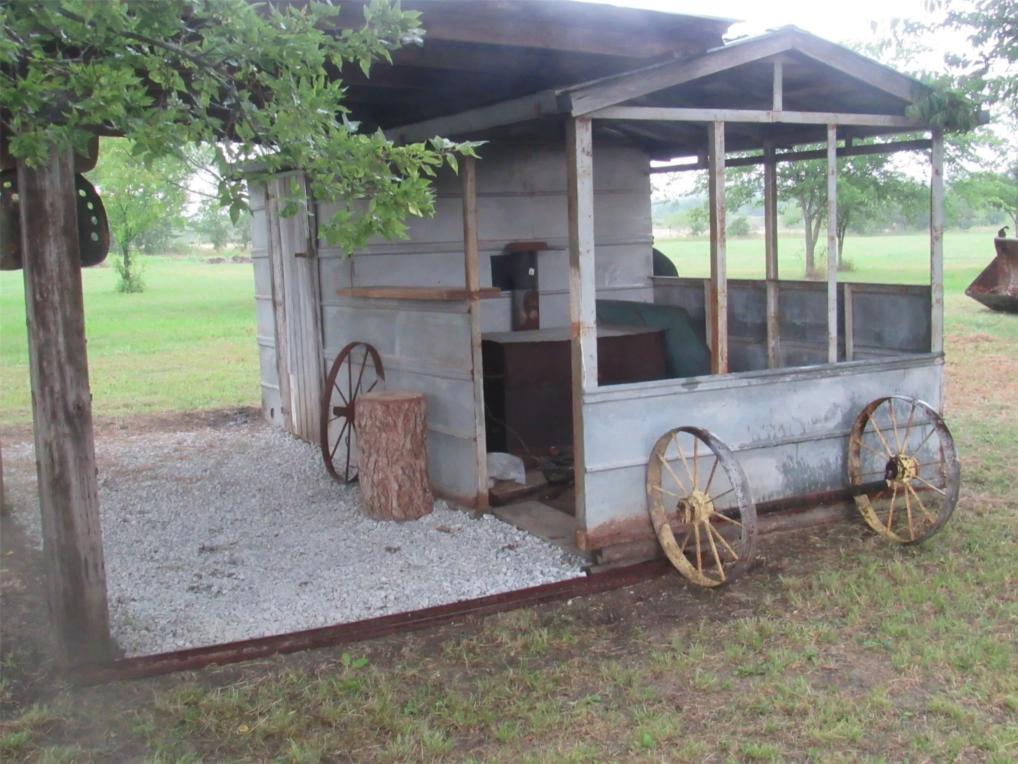 Outdoor structure with a pitched roof and open-air front, gravel flooring, and decorative wagon wheels