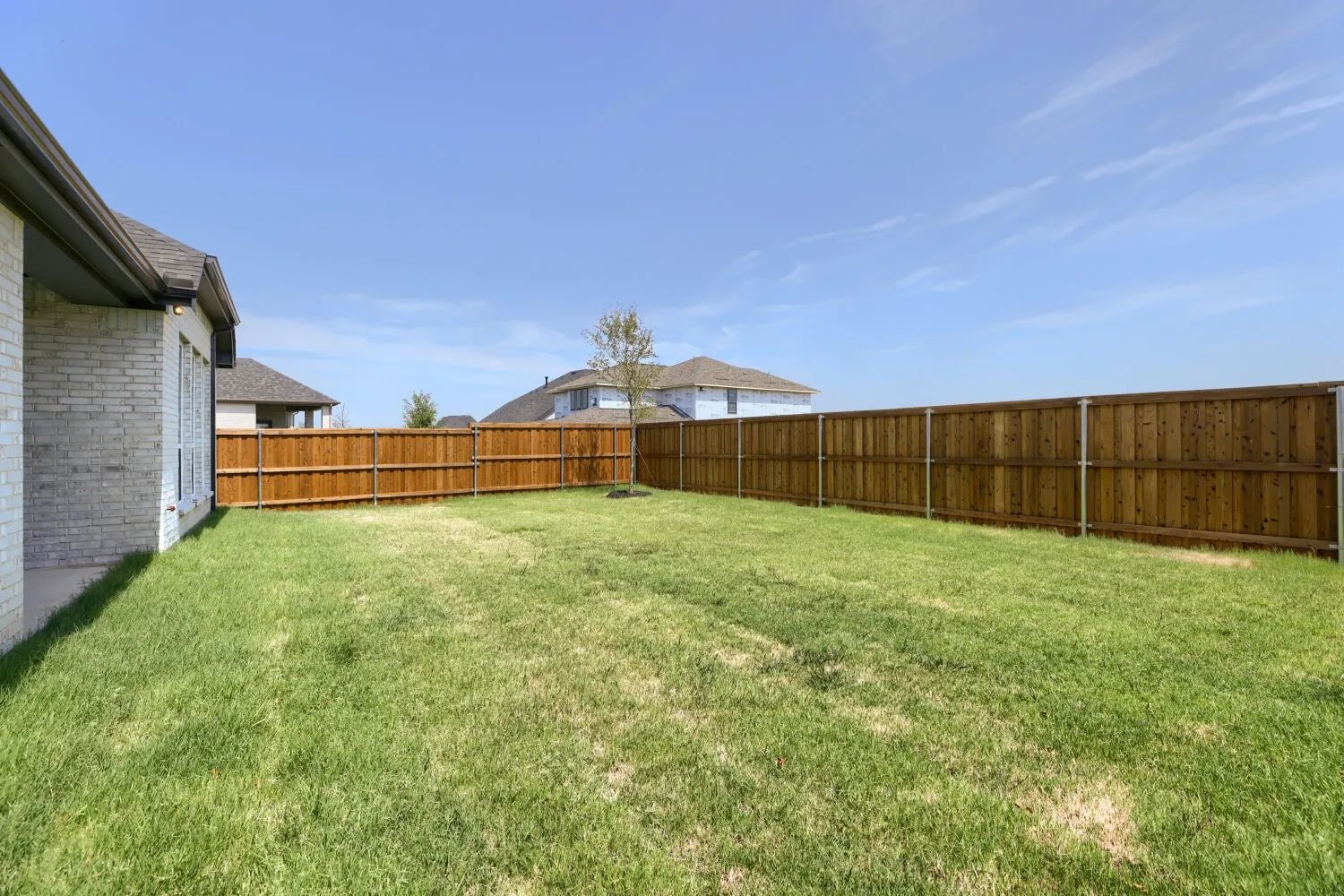 Expansive backyard with a manicured lawn, full wood privacy fencing, and a mature tree