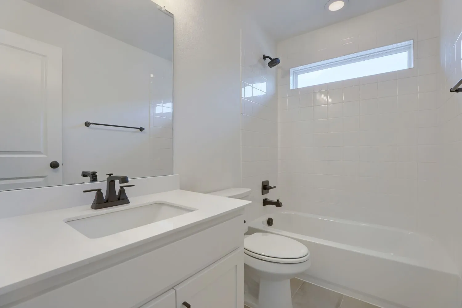 Modern bathroom featuring a white quartz countertop with an integrated rectangular sink, matte black faucet and hardware, large framed mirror, and a separate soaking tub with tile surround