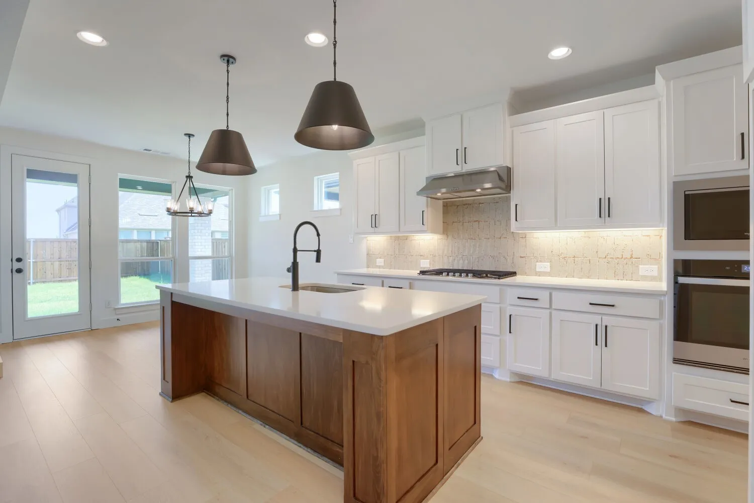 Chef's kitchen featuring white cabinetry with brushed nickel hardware, a wood-finish island with quartzite countertops, stainless steel double wall ovens, gas cooktop, subway tile backsplash, and pendant lighting