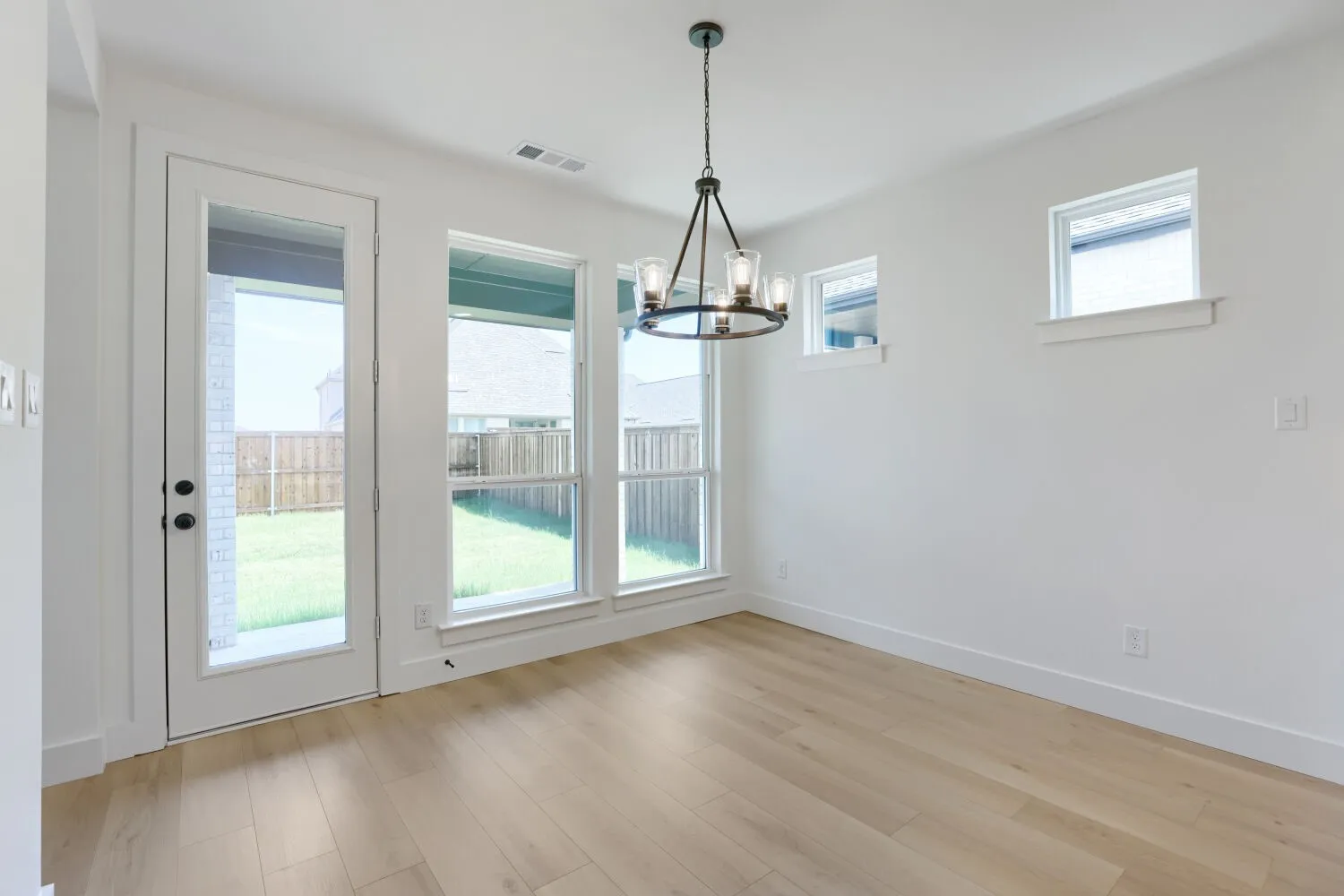 Light wood-finish flooring, multiple windows, a glass-paneled door, and a black metal chandelier