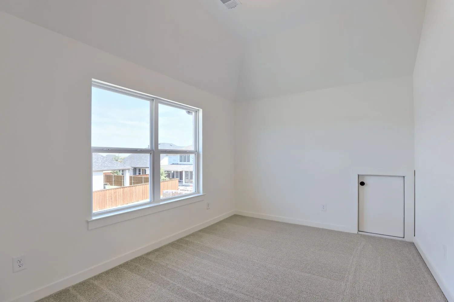 Vaulted ceiling, large window, neutral carpeting, white walls, and a small access door