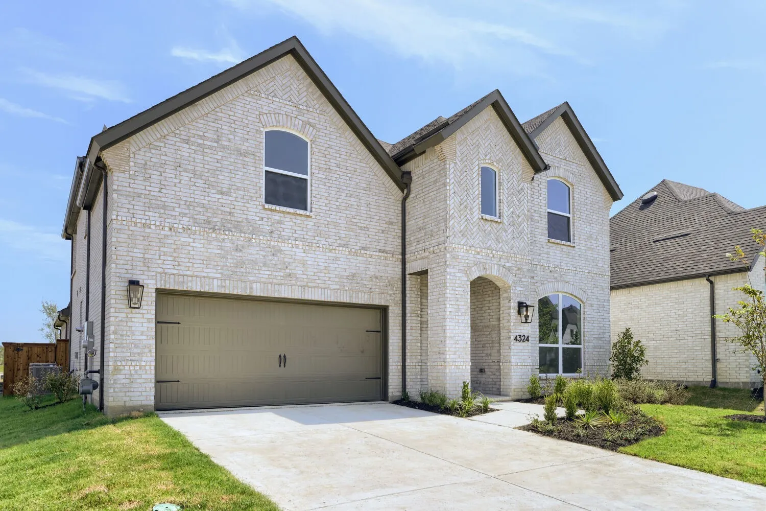 Brick exterior with dark trim accents, arched entry, two-car garage, concrete driveway, and front landscaping