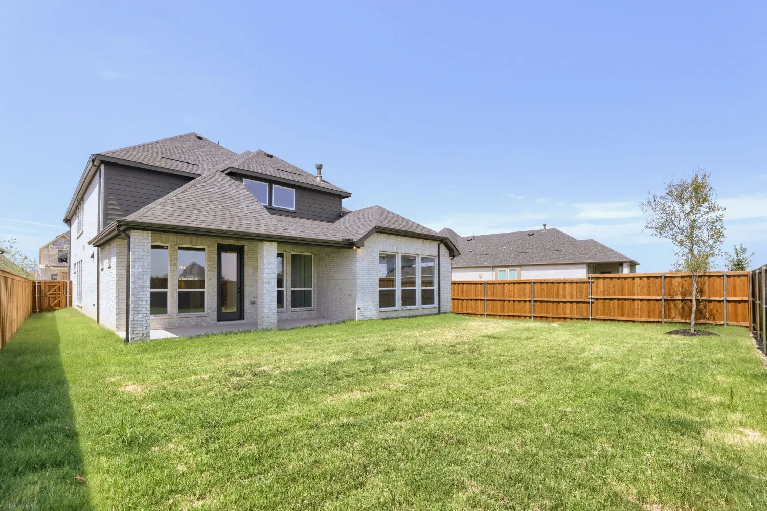Contemporary two-story residence with multi-pane glass doors and windows, composite or fiber cement siding in neutral tones, and an asymmetrical roofline with multiple peaks