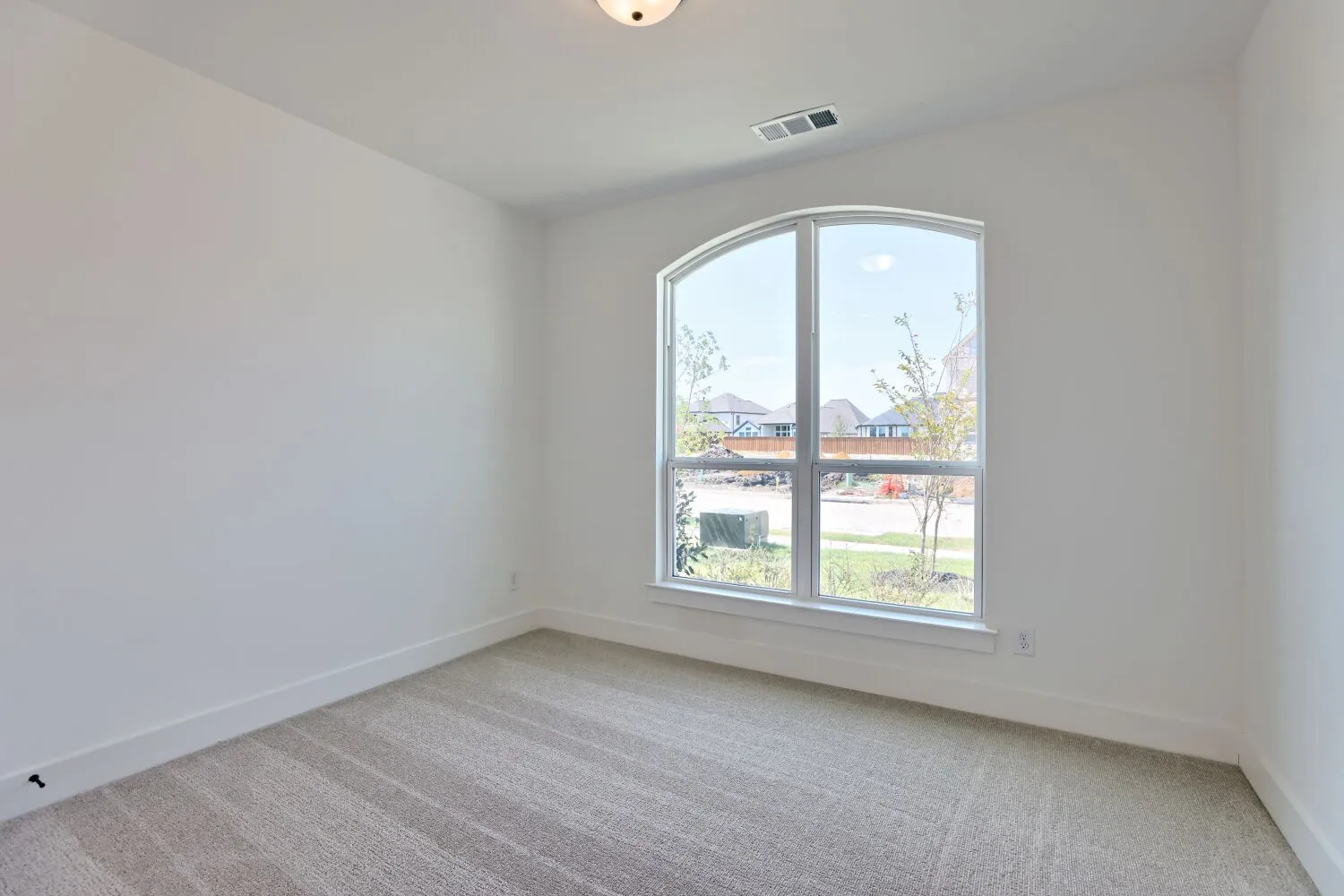 Bright corner bedroom featuring a large arched window with multiple panes, neutral wall finishes, and plush carpet flooring