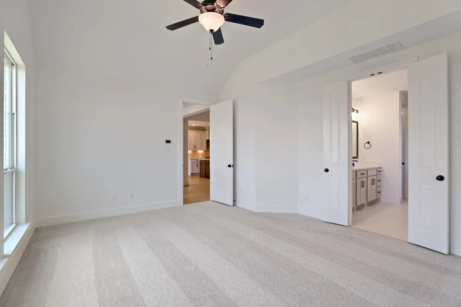Vaulted ceiling, ceiling fan, neutral carpet, white paneled doors, and a window