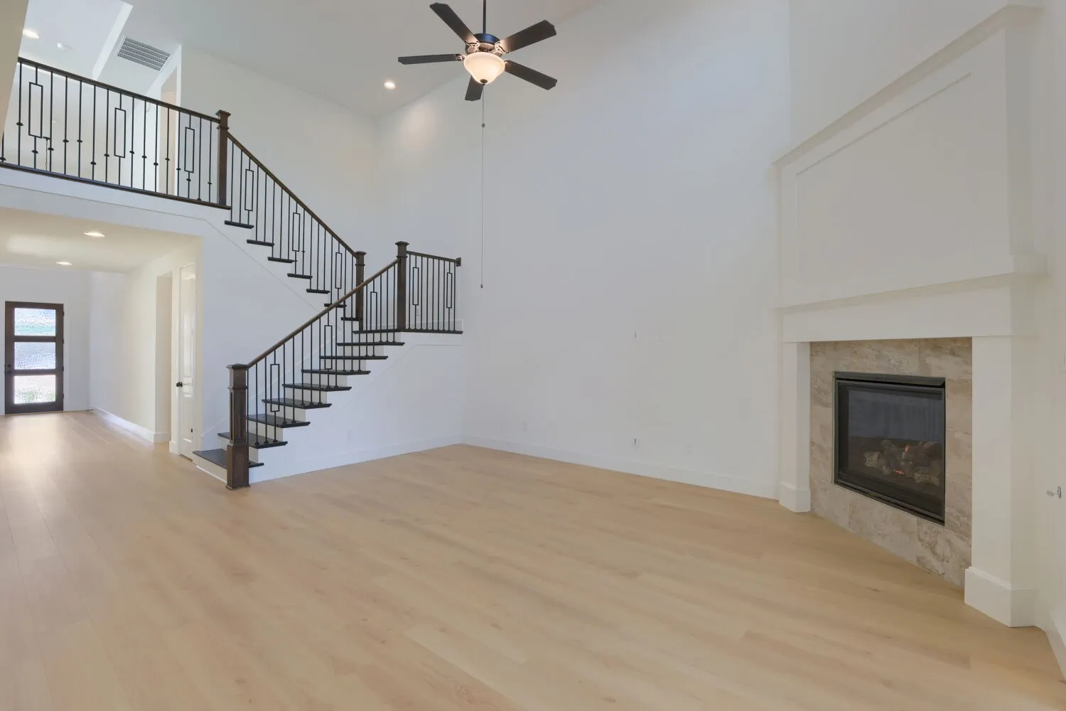Vaulted ceilings, a decorative iron staircase, light wood-finish flooring, and a fireplace with a stone surround