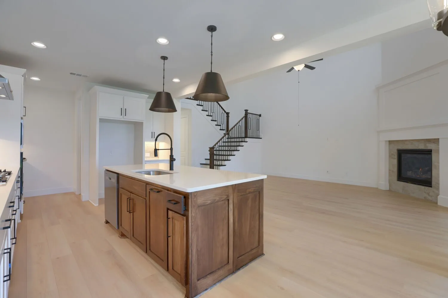Kitchen island with sink and stainless steel dishwasher, light wood-finish flooring throughout, two-story ceiling with a modern fireplace, white cabinetry, and recessed lighting