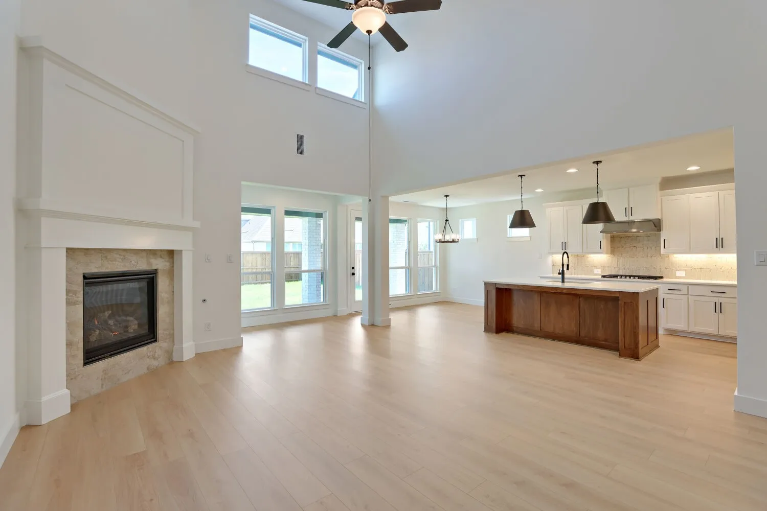 Open-concept living space featuring soaring ceilings with skylights, a wood-finish plank floor throughout, and a gas fireplace with white surround