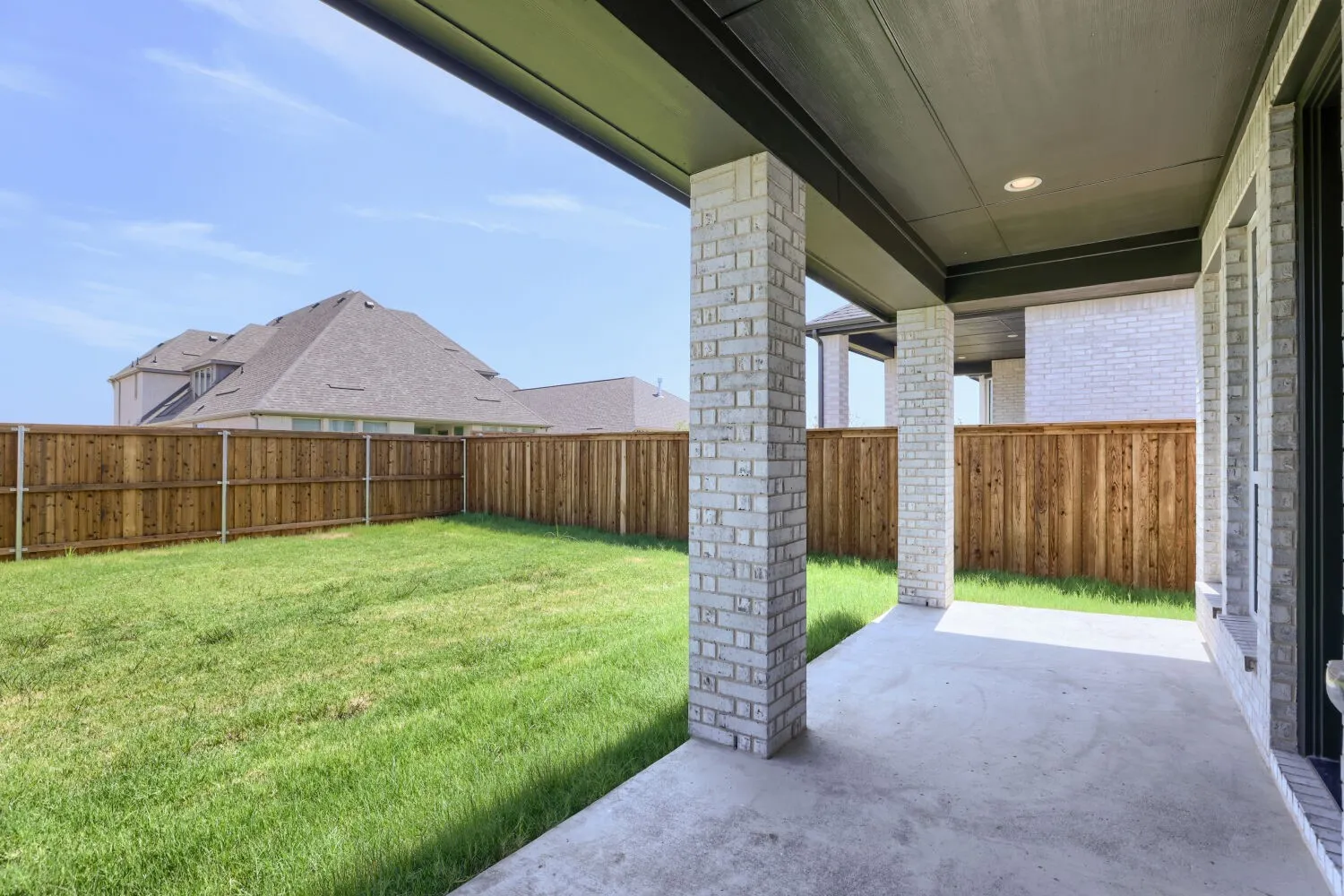 Expansive backyard retreat featuring a manicured lawn, wood-finish privacy fencing, and a covered patio with concrete flooring