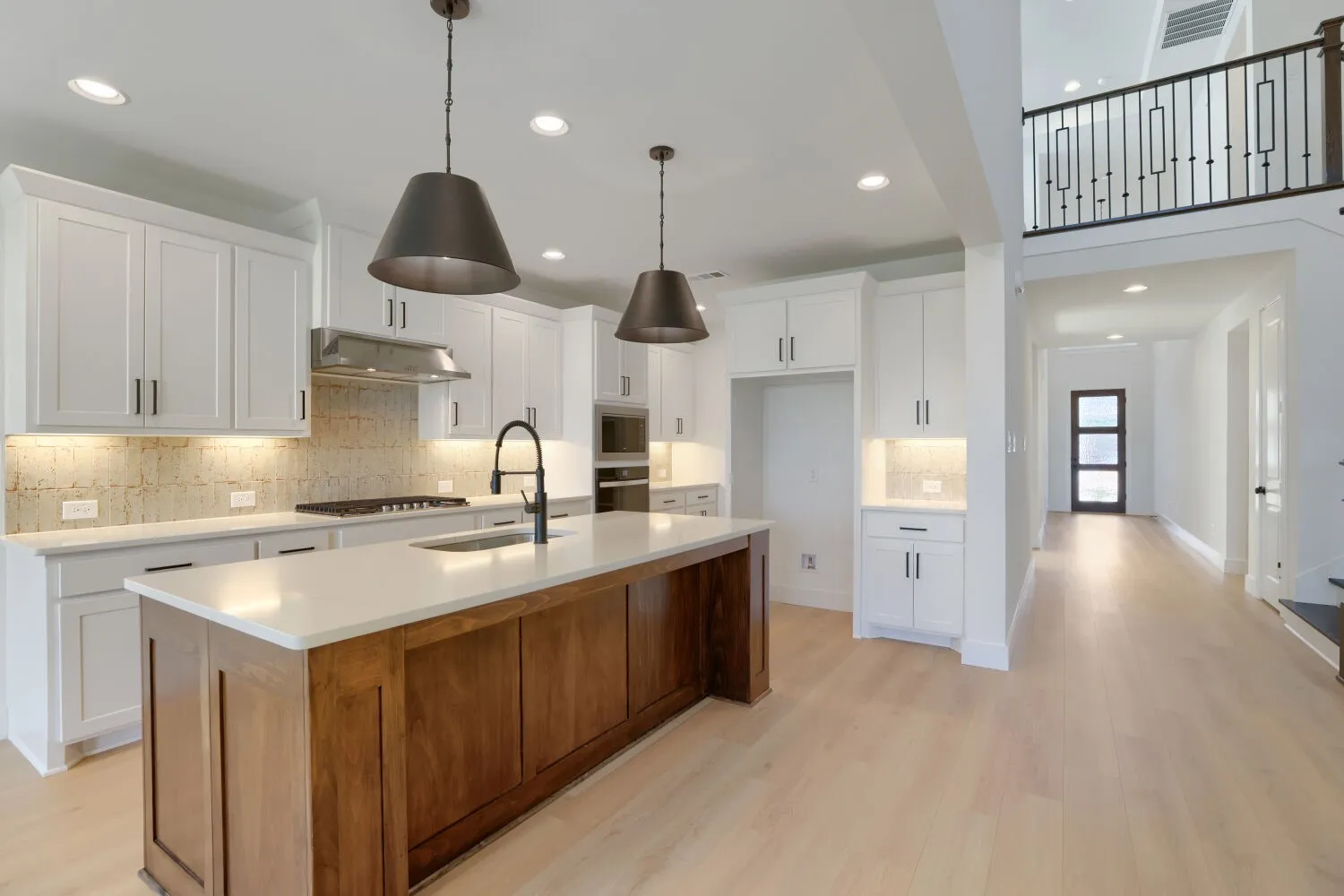 Open-concept kitchen featuring white shaker cabinetry, a wood-finish island with a light-toned countertop, and stainless-steel appliances