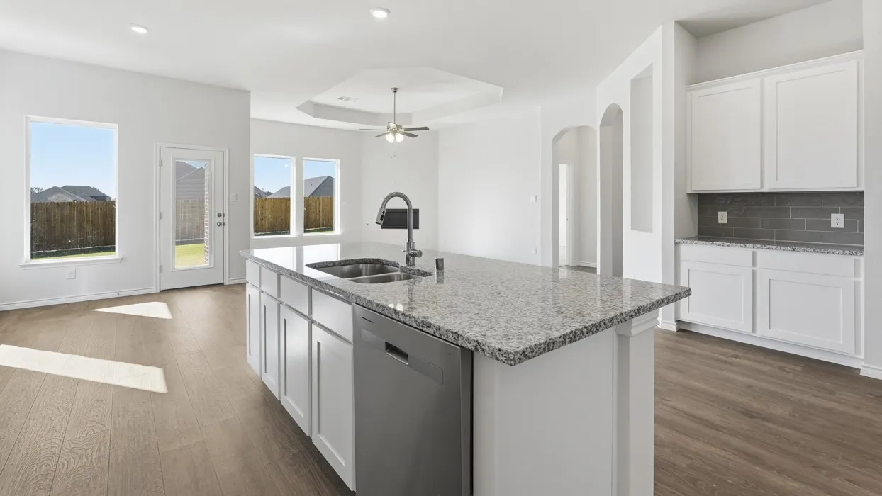 Bright, open-concept kitchen featuring a large center island with white cabinetry, gray quartz countertops, and stainless steel appliances