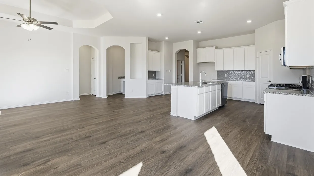 Open-concept kitchen and living area featuring white cabinetry, a large island with seating, stainless steel appliances, tile backsplash, and wood-finish flooring throughout