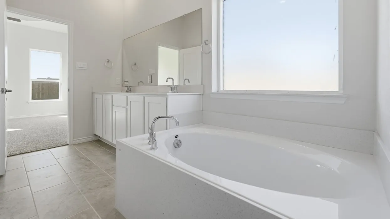 Spa-inspired primary bathroom featuring a freestanding soaking tub with chrome fixtures, dual-sink vanity with white cabinetry and integrated countertop, large framed mirror, and abundant natural light from an expansive window