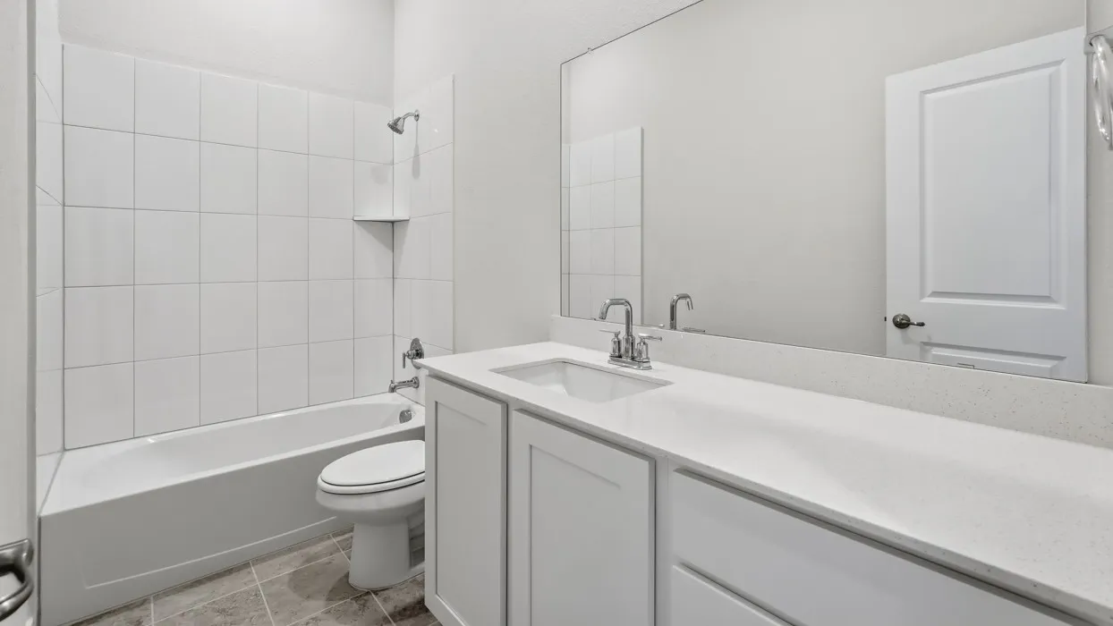 Bright and functional bathroom featuring a white subway tile shower surround, ceramic toilet, and expansive double vanity with white cabinetry and quartz countertop