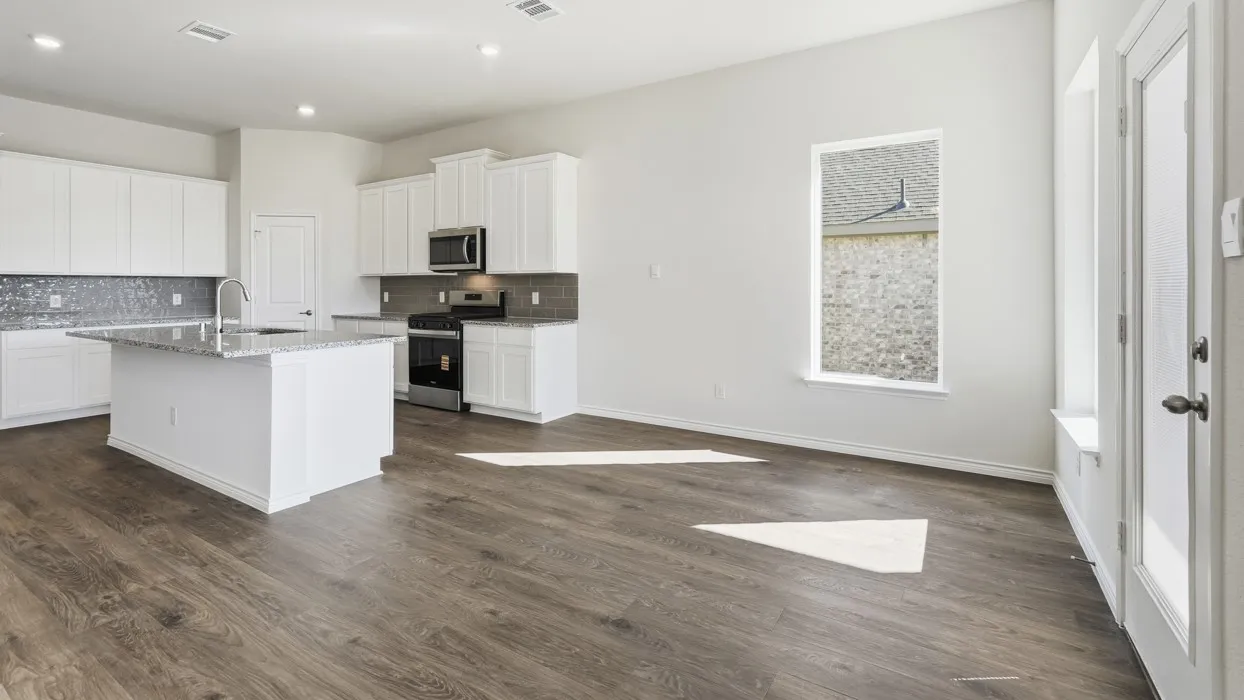 Open-concept kitchen and living area featuring wood-finish flooring, white cabinetry, a kitchen island with seating, a stainless steel microwave, and a glass-paneled door