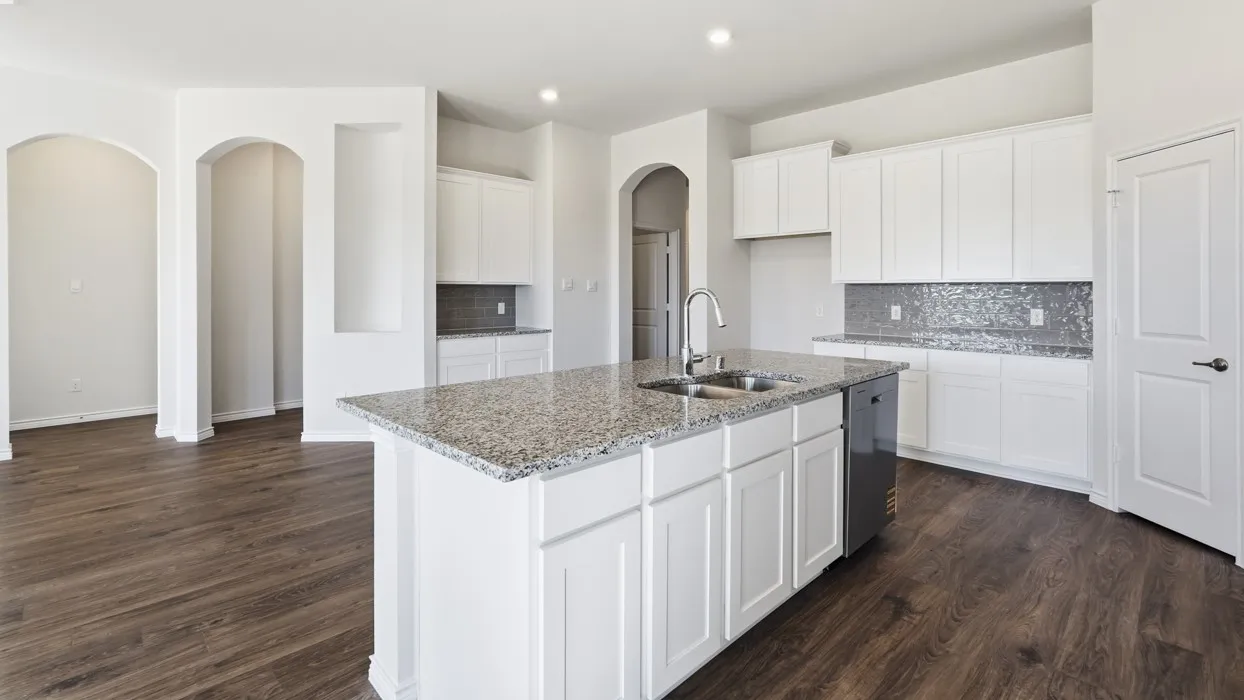 Spacious kitchen featuring white cabinetry with arched doorways, a large center island with speckled granite countertops, stainless steel appliances, a mosaic tile backsplash, and wood-finish flooring throughout the open layout
