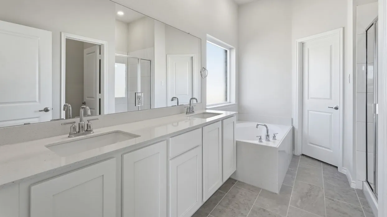 Spa-inspired primary bathroom featuring a dual-sink vanity with white cabinetry, quartz countertops, and polished chrome fixtures