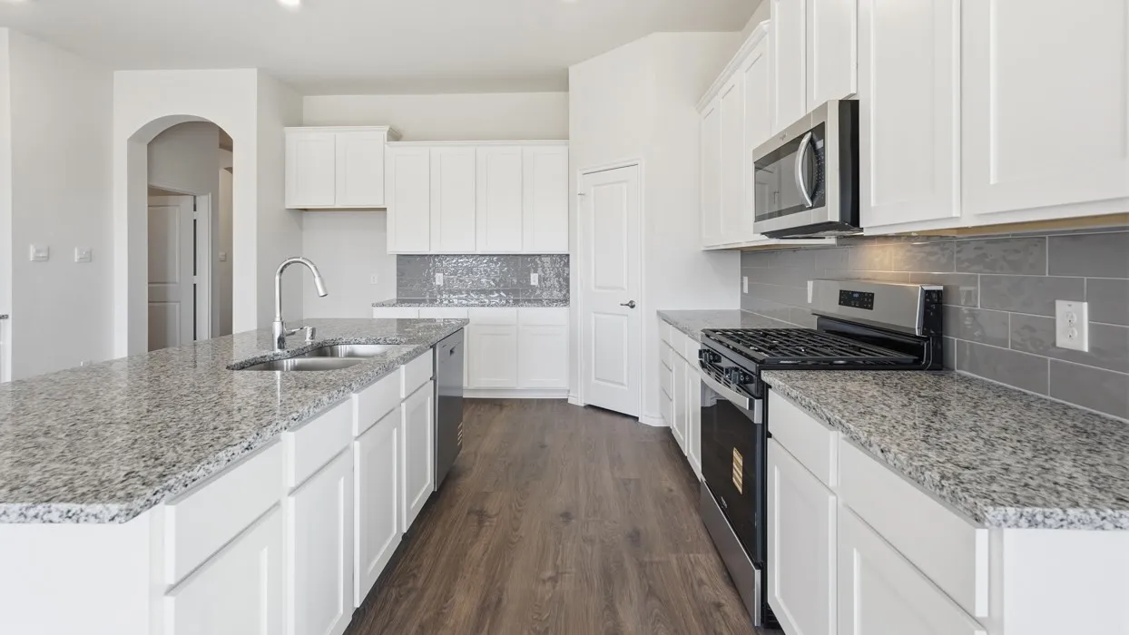 Galley kitchen featuring white cabinetry, granite countertops, stainless steel appliances including a gas range and built-in microwave, subway tile backsplash, and wood-finish flooring throughout the open layout
