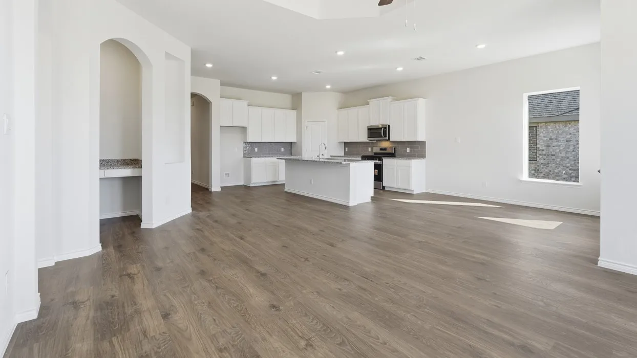 Open-concept living area featuring wood-finish flooring, recessed lighting, and a white kitchen with an island, stainless steel appliances, and a tiled backsplash